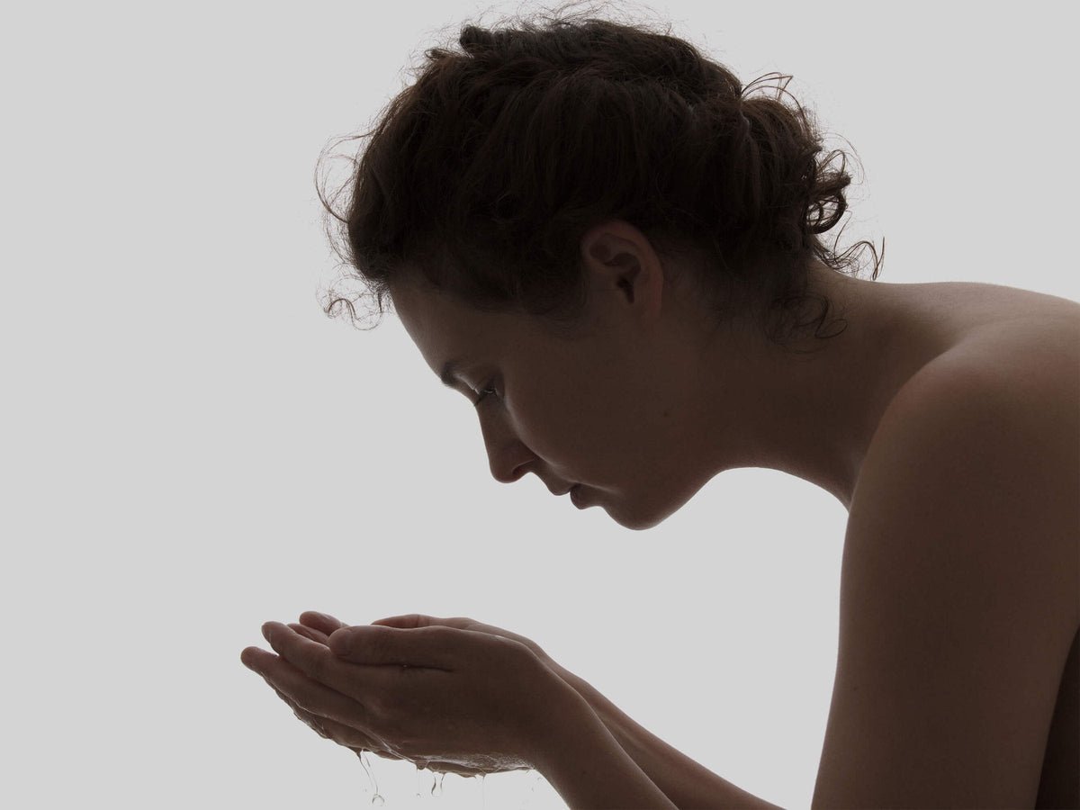 Frau wäscht ihr Gesicht mit warmem Wasser, bevor sie das Less Face Oil aufträgt
