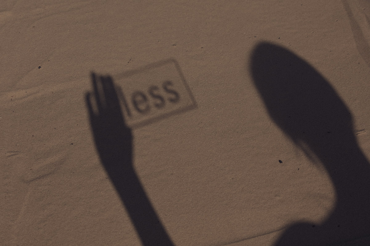 Schatten einer Frau in der Sonne neben dem Schriftzug less im Sand